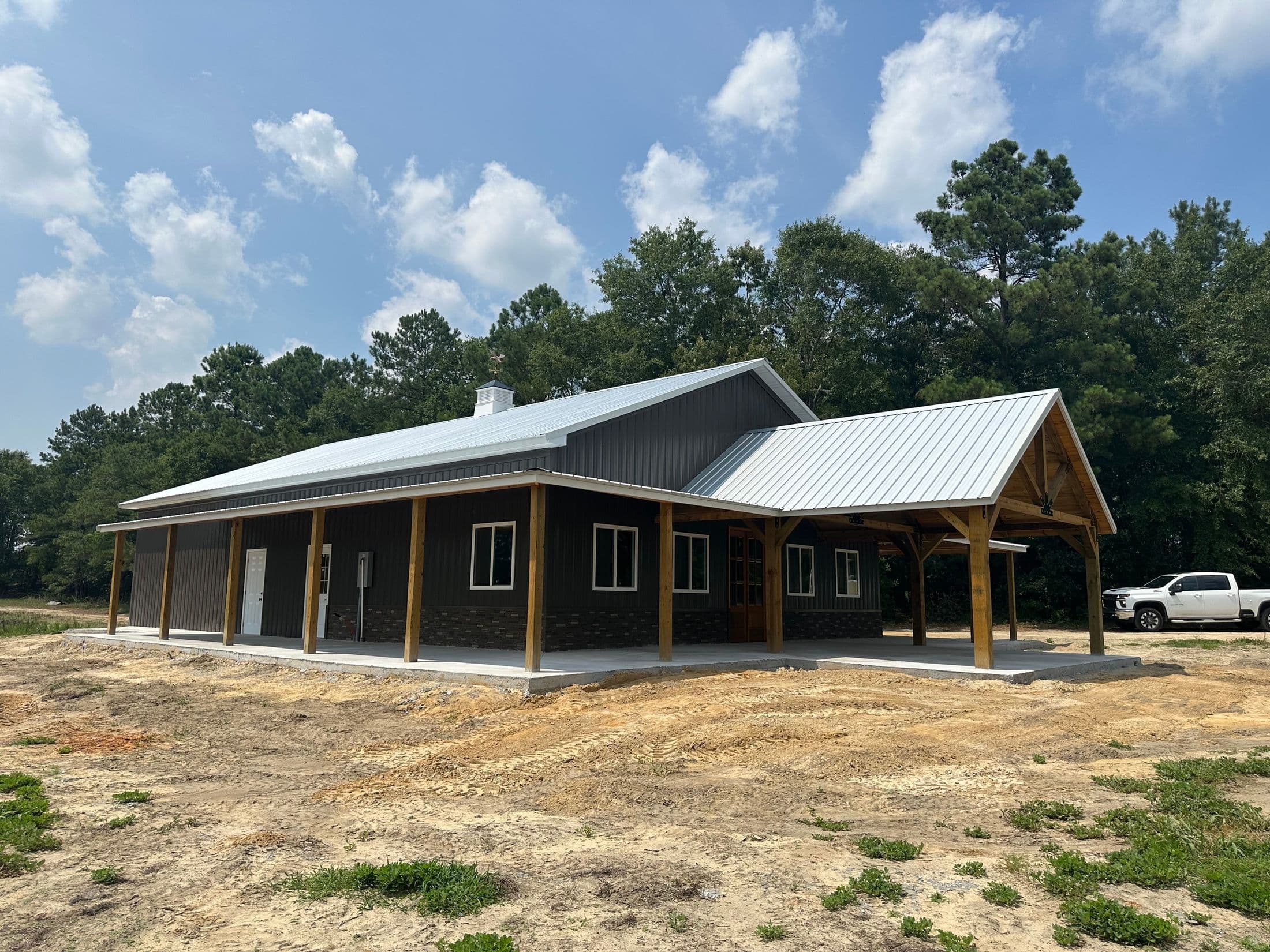 Brown barndominium with wraparound covered porch and standing-seam metal roof