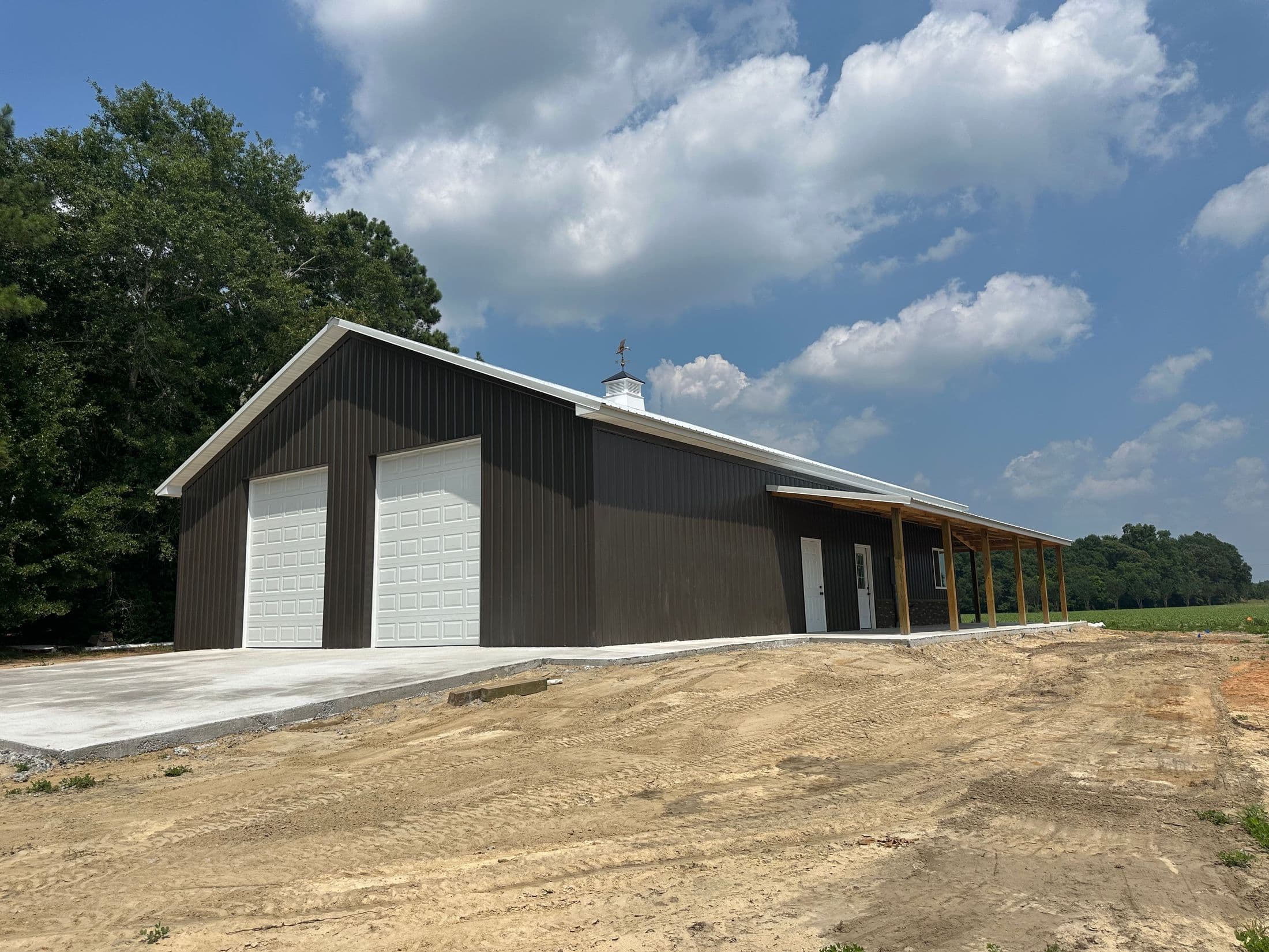 Dark brown pole barn with two white overhead doors and a covered lean-to porch