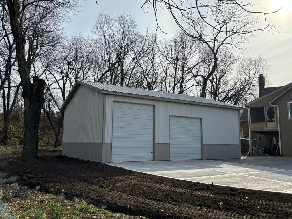 Two-tone gray pole barn garage with two overhead doors beside a home